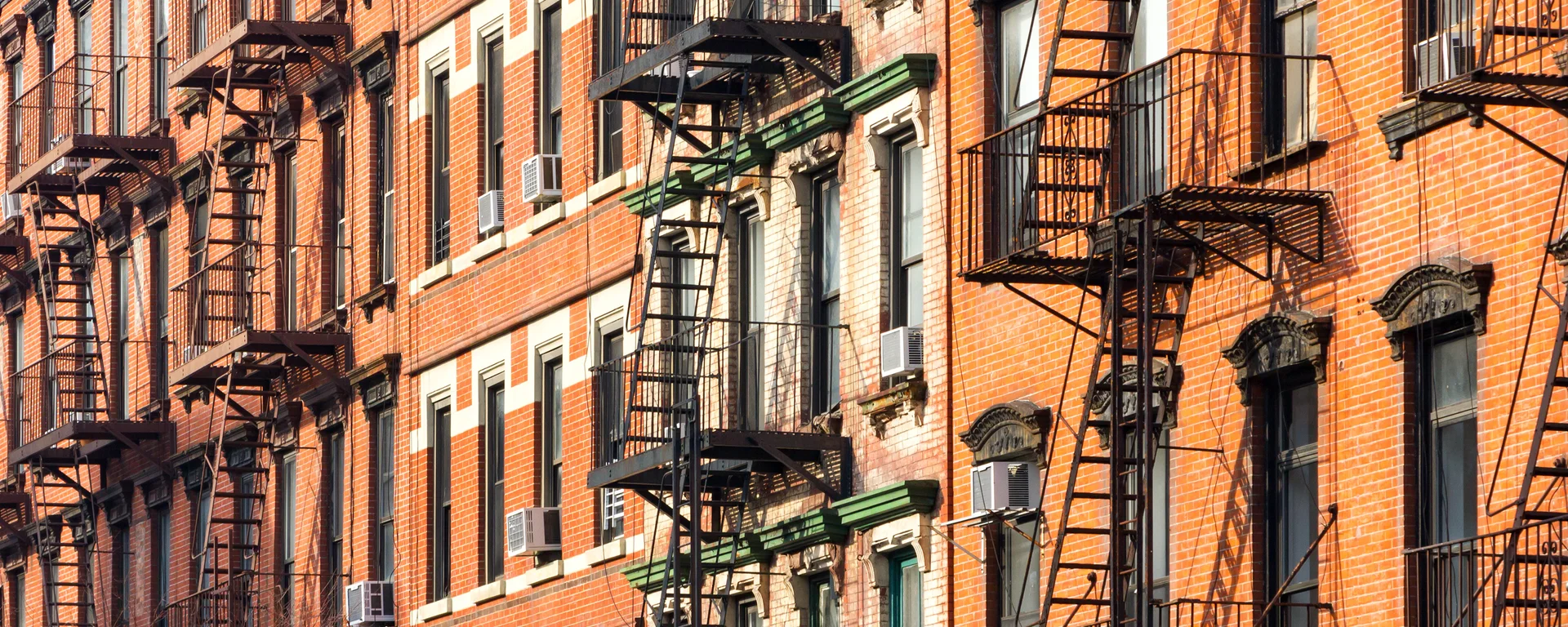Fire escapes and window rows on brick tenement facades in the Bronx, in low sun.